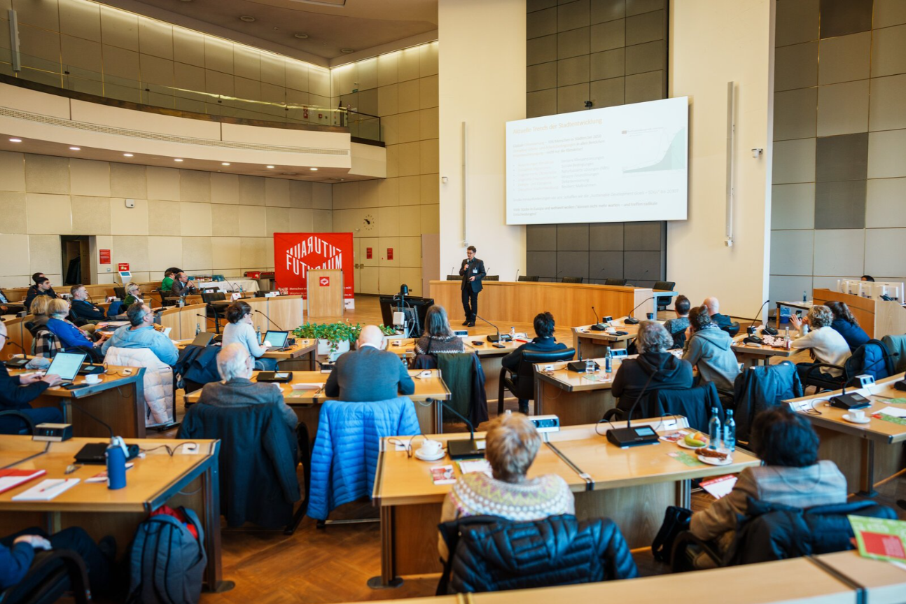 Personen sitzen im Ratsaal und hören Sprecher zu