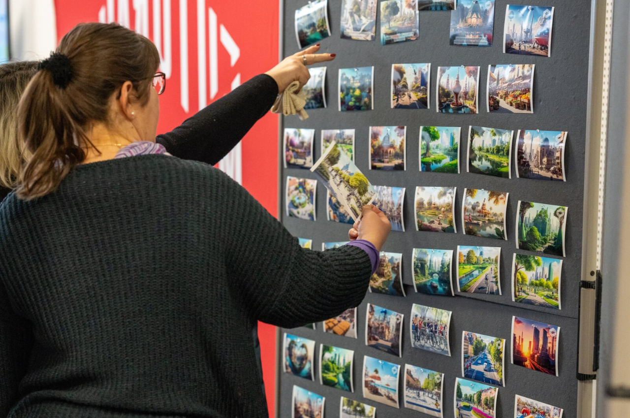 Zwei Frauen zeigen auf eine Pinnwand, auf der von KI entwicklte Fotos hängen