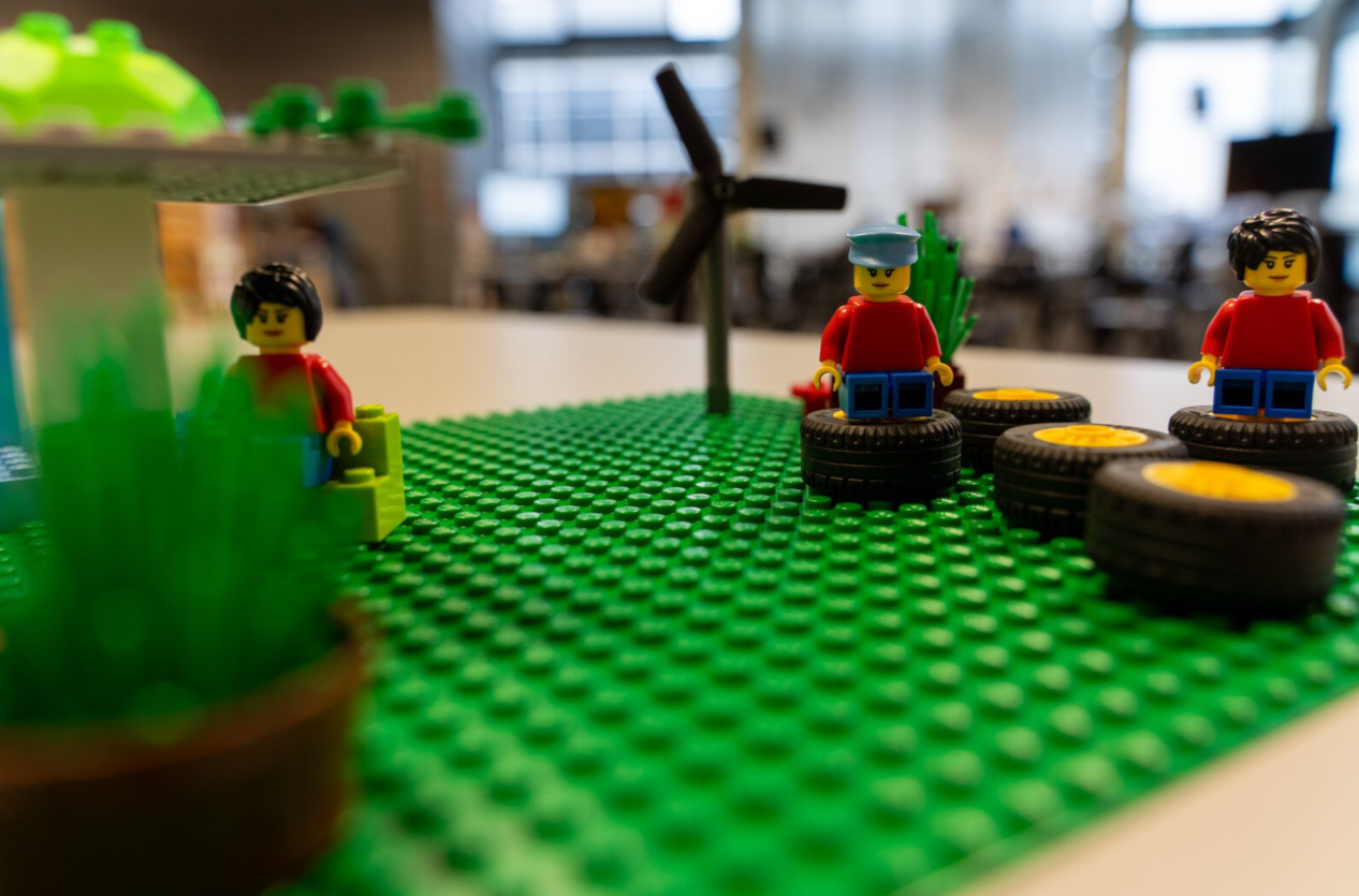 Aus Lego gebaut: Grüne Landschaft mit Windrad und Personen, die auf Reifen sitzen